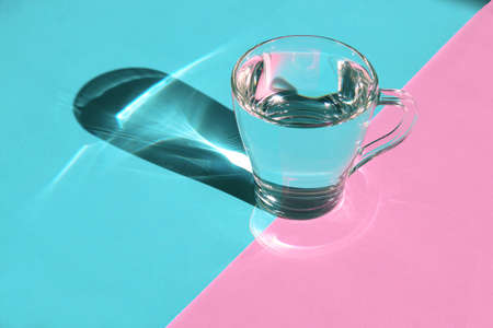 Glass cup of water with hard shadows on blue pink background.の写真素材