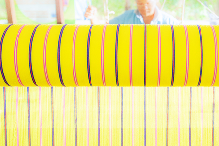 Thai women weaving cotton cloth with traditional hand loom, unique identities of northeastern Thailand. Bright sunlight. Weaver background. Selective focus. Warm tone.の写真素材