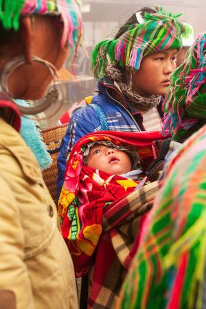 Sa Pa, Vietnam - FEBRUARY 27, 2012: Tribe Hmong baby infant open beautiful eyes and looking around hmong family. Hmong women vendor in traditional clothing selling souvenir with family. Sa Pa.のeditorial素材