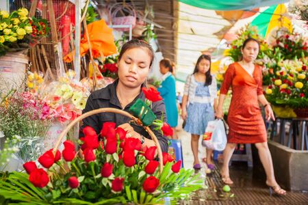 Phnom Penh, Cambodia %u2013 SEPTEMBER 22, 2013: Khmer florist woman making beauty bouquet of red roses on the footpath. Phsa Thmei Market.のeditorial素材