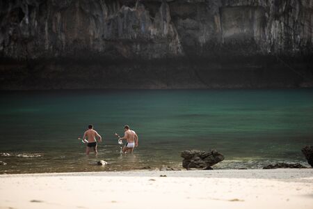 Couple tourists with snorkel in blue sea in front of ancient cliff. Sunny day white sand beach foregrounds. Summer season. Koh Hong Island, Andaman sea, Krabi, Thailand. Soft sunlight. Copy space.の写真素材