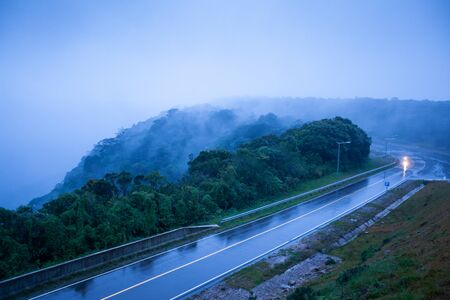 Mountain road in foggy dusk, motorcycle riding on asphalt road through the mountain top of Phnom...