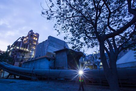 Cement plant factory manufacturing at dusk, sparks of worker with headlamp flashlight during working...