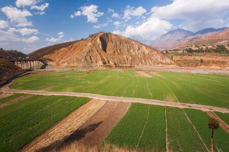 Aerial view, landscape of vegetable field in the valley of Yunnan, China, farmer harvesting lush vegetable in rows, beautiful view, brown mountain range with snow ridge, light blue sky. Spring season.の写真素材