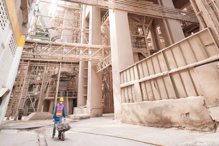 Male asian laborer wearing safety protective gear with sewage inside a wheelbarrow at cement factory. Hard work concept.の写真素材