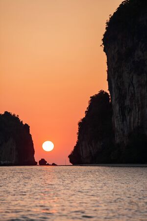 Relaxing time, scenic seascape at dusk, colorful sun setting over the island. The orange sun with a soft orange glow blankets the sky as surface seawater. Summertime. Libong Island, Trang, Thailand. Silhouette.の写真素材