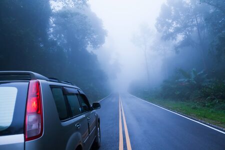 Rear view of silver SUV car on the asphalt road while through a misty mysterious tropical forest. Somewhere in North Thailand. Adventure concept. Selective focus.の写真素材