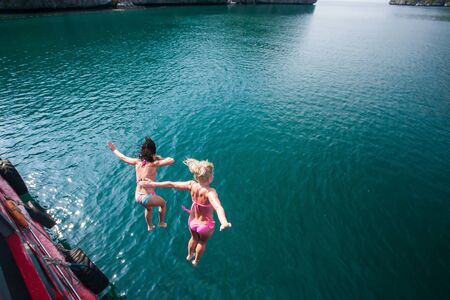 Motion blur, couple happy girl friends in bikini jumping of wooden boat into the sea, tropical islands backdrop. Summer holiday lifestyle.の写真素材