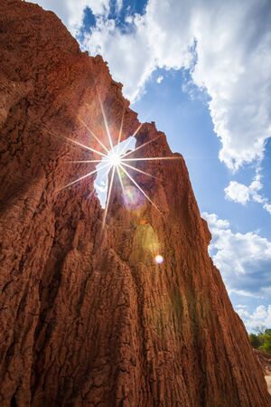 Fantastic steeply sedimentary red sand in a desert, sunny star ray, clouds with light blue-sky...