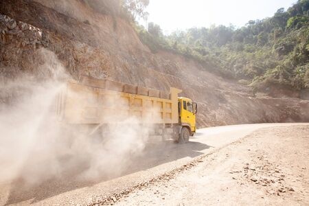 The yellow dump truck working on the dusty mountain road at construction site, a new road construction in North Laos near Laos-Vietnam border. Development project.の写真素材