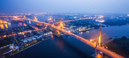 Soft focus, aerial view of Bhumibol Suspension Bridges and highways interchange over the Chao Phraya River at dusk, beautiful light trails across the bridges and river curve. Samut Prakan, Thailand.の写真素材