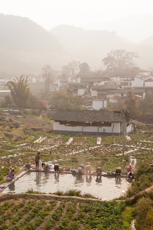 Peaceful village. Scenic ancient village landscape, a group of chinese woman washing at the old pool in potatoâs field in the mist. Mountains in the mist backgrounds. Yunnan, rural of South China. Soft morning light.のeditorial素材