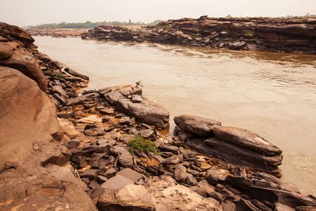 A local fisherman casting the fishing net in the Mekong River, fantastic scenery of steep sandstone cliff by the river on summer evening, rural life near Thailand-Laos border.の写真素材