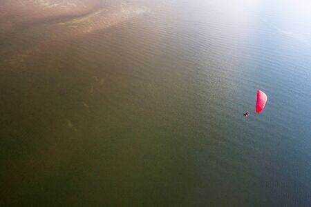 Red paramotor by the sea, top view of red paramotor flying over the sandy on the tropical sea,...