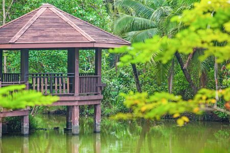 Brown wooden gazebo in a pool garden, lush and green shady of branches of tropical trees, tropical pool garden in summer.の写真素材