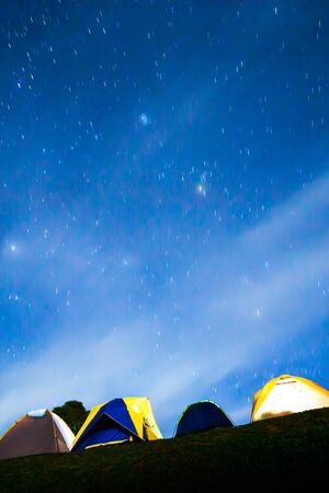Picturesque illuminated camp tents under the starry night sky, camping on the mountain high in winter. Soft focus.の写真素材
