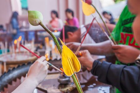 Asian buddhist devotees holding lotus flowers with artificial golden sacred fig leaf to paying respect to buddha. Close. Focus on artificial golden sacred fig leaf.の写真素材