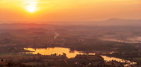 Picturesque aerial view of lake with the sun setting over a mountain range in background, winter...
