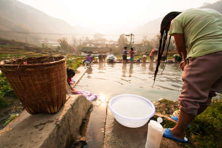 A group of chinese women showering and washing at the stone pool in ancient village at sunrise, rural scene in Yunnan, South China.のeditorial素材