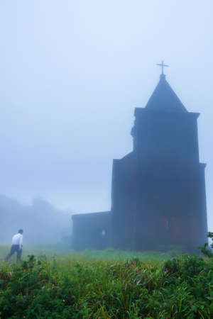 A male Khmer walking toward the abandoned ancient church in the mist, the church was built from the...