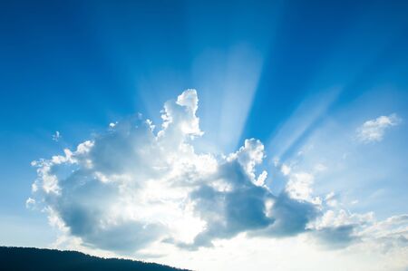 Sunbeams shines through the cloud over a mountain range, dramatic light beams illumination against blue sky in the background. Inspiration concept.の写真素材