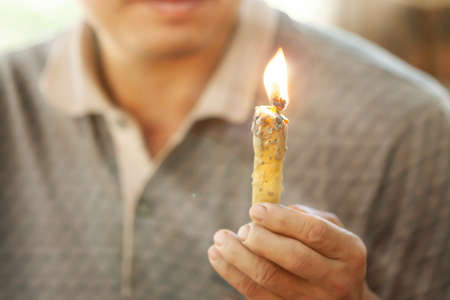 An Asian male farmer holding a candle, a candle made from organic beeswax, living the simple life in a farm in North Thailand. Soft focus on candle.の写真素材