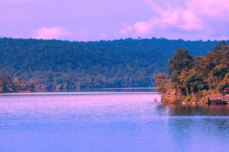 Male fisherman fishing on a tranquil lake at sunset, dramatic sunset sky reflection on the lake. Soft focus on the lake.の写真素材