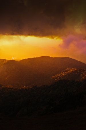 Dramatic rainstorm hiding the setting sun and mountain ridge, magical spotlight shines through dark clouds onto the mountains. Focus on mountains.の写真素材