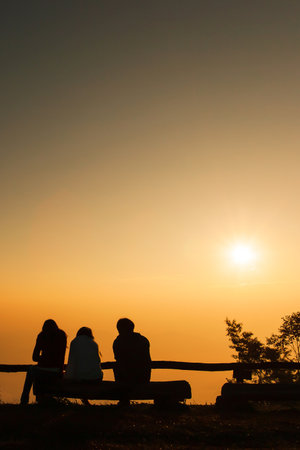 A group of tourists sits on the logs at viewpoint while  relaxing on a mountain peak at sunrise, the rising sun over a mountains in the backgrounds. Holiday, Vacations concepts.の写真素材