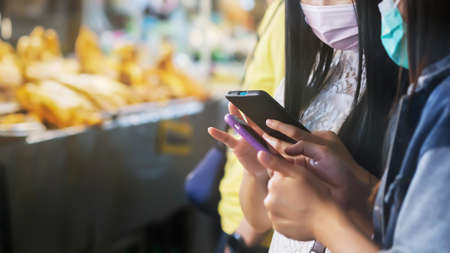 Two Asian women wearing face mask holding smartphones choose and looking for things to buy in a...