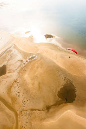 Aerial view of red paraglider flying over an island. Wavy sand beach texture, blue sea and green mangrove forest in the backgrounds. Trang, Thailand. Focus on paraglider.の写真素材