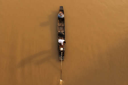 Aerial view an Asian fisherman stands on traditional wooden fishing boat while casting fishing net on a river at sunrise. Rural scene in Thailand. Focus on fisherman.の写真素材