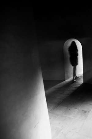 Unknown female walks alone in the dark ancient basement with the light at the end. Sunbeam shines through tunnel onto the staircase. Motion blur.の写真素材