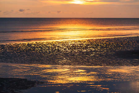 A tranquil summer beach at sunset. Dramatic sunset sky reflection on a tropical beach and ocean waves. Chanthaburi, Thailand. Tourism, holiday, vacations concepts. Focus on the beach.の写真素材
