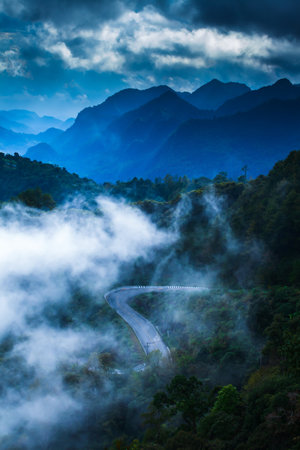 Scenery of mountain road in the morning mist. Stunning view of curves mountain road in foggy, rain clouds covers mountains range in the backgrounds. Tourism, road trip, holiday concepts. Soft focus.の写真素材