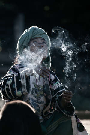 Chiang Mai, Thailand - DECEMBER 21, 2010: An elder Lahu tribe woman in traditional clothing smoking cigarette in sunlight. Omkoi.のeditorial素材