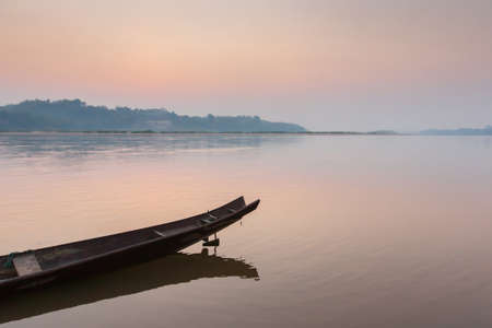 A traditional wooden boat on the Mekong Riverbank at dawn, sunrise sky reflection on surface of the river. Thailand-Laos border. Focus on the boat.の写真素材