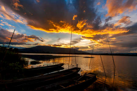 Scenery of a lake at dusk, dramatic clouds and sunset sky over a lake and mountains in the backgrounds, a local dock with wooden boats in the foreground. Loei, Thailand. Focus on a lake.の写真素材