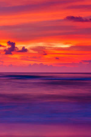 Seascape view of a tropical beach during sunset. Colourful sunset sky and ripples clouds reflection on surface of ocean waves and the beach. Long exposure. Motion blur.の写真素材