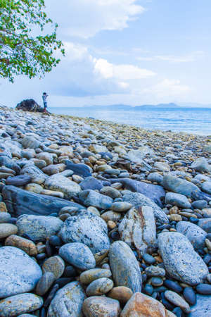 Seascape view of the tropical pebble beach on sunny summer, a tourist man stands in the background. Kang Kao Island, Ranong, Thailand. Focus on the pebbles.の写真素材