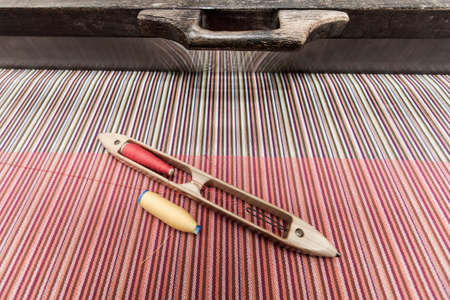 Thai traditional wooden weaving loom and weaving shuttle with colors sewing thread on woven cotton. Close-up. Top view.の写真素材