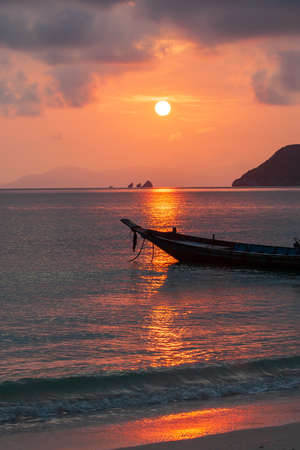 A tranquil seascape view of the tropical beach and a wooden fishing boat at sunset. Koh Wua Ta Lap Island in summer, Surat Thani, Thailand. Tourism, holidays, vacations.の写真素材
