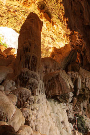 An Asian young man in casual wear stands and looks at the large stalagmite in the limestone cave. Koh Wua Ta Lap Island, Thailand. Focus on the stalagmite.の写真素材