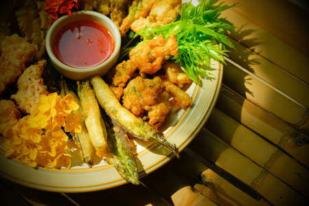 Deep-fried tropical flowers, leaves, and vegetables served on a white plate, flat lay on the bamboo table. Healthy food. Top view. Close-up. Selective focus.の写真素材