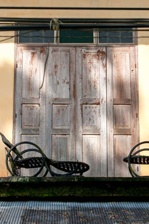 Vintage chairs are on the balcony of an old house. Sunlight shines on cream concrete walls with wooden doors in the background.の写真素材