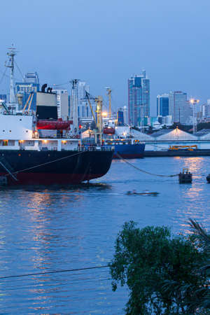 Liners, cargo ships, and container ships dock near the Bangkok Port at dusk, with local wooden boats and other boats passing by. Chao Phraya River, Thailand.の写真素材