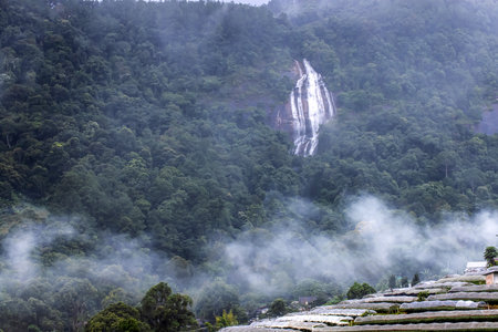 The landscape of a waterfall falling from a mountain with flowers terraces fields and a local village, soft fog drifting over a valley. Doi Inthanon, Chiang Mai, Thailand.の写真素材