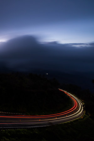 Driving on a mountain road during a heavy storm, illuminated light trails against dark thunderstorms in the background. Transportation, travel concepts.の写真素材