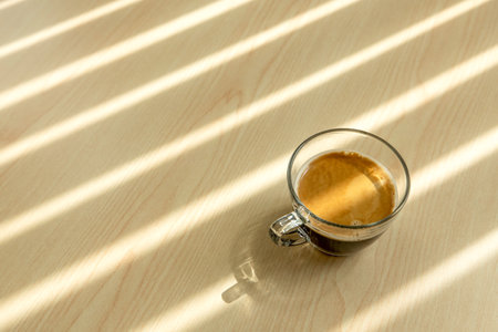 A close-up of a cup of coffee is on the wooden table, shadow-striped through the window onto the table. Flat lay. Top view.の写真素材