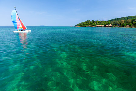 A sailboat sailing in the blue sea near a tropical island on a sunny summer. South Thailand.の写真素材
